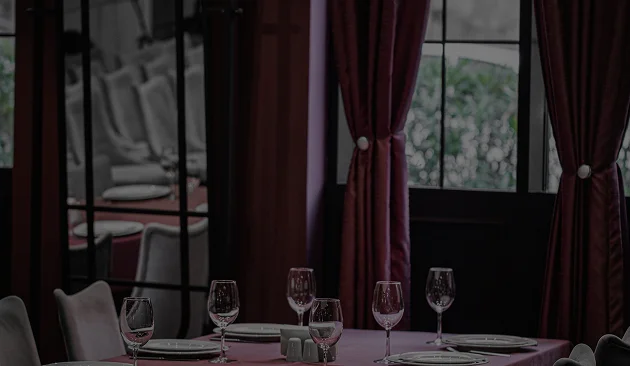 Une table à manger élégamment dressée, avec une nappe rouge, des verres à vin et des serviettes pliées, dans un restaurant raffiné aux rideaux sombres.